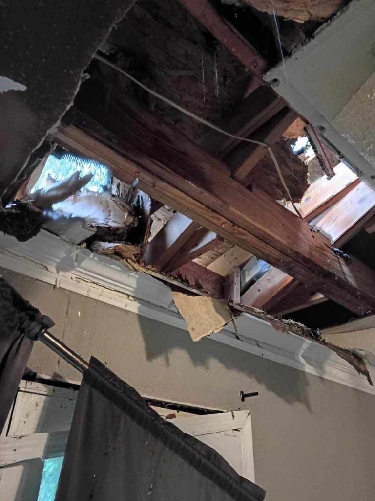 Hole punched through the interior ceiling exposing wooden rafters, insulation, and daylight.