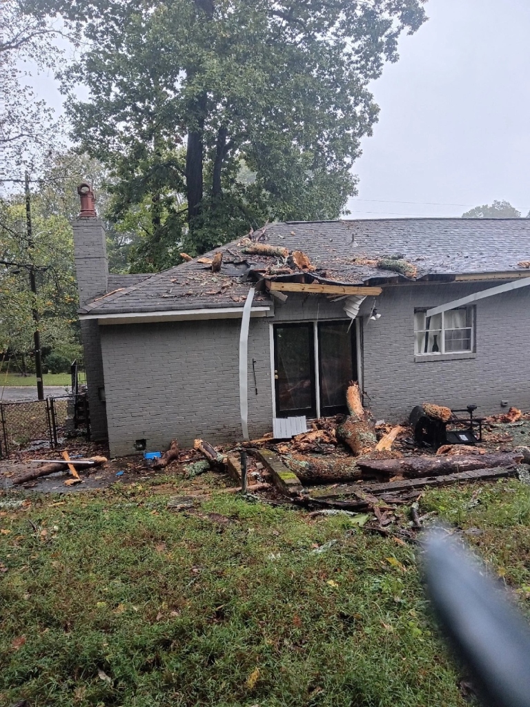 Wide exterior view showing the fallen oak tree across the roof, crushed gutter, and debris.